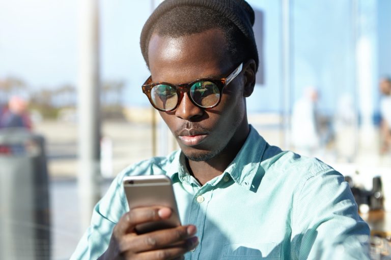 Indoor portrait of serious concentrated Afro American young man reading urgent text message on mobil